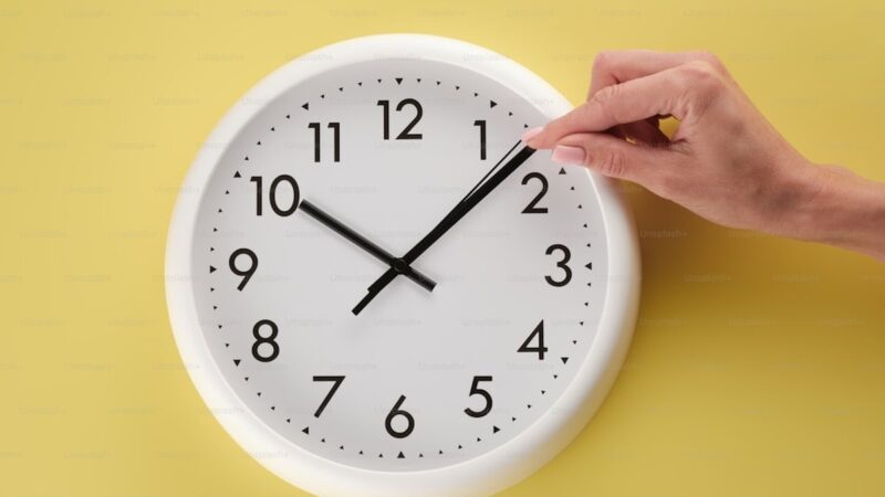 A person holding a white clock on a yellow wall