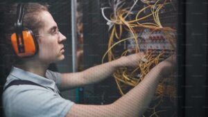 Side view of young network engineer connecting cables in server room during maintenance work in data center, copy space