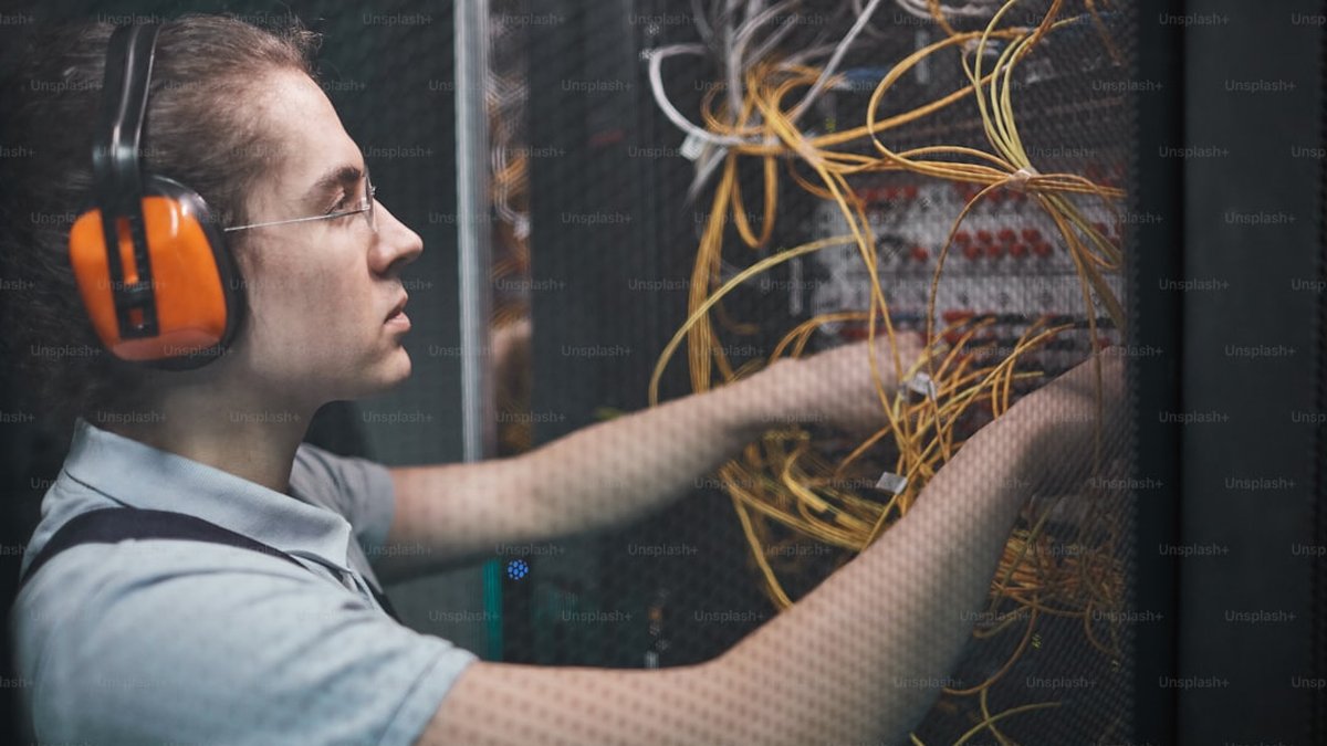 Side view of young network engineer connecting cables in server room during maintenance work in data center, copy space